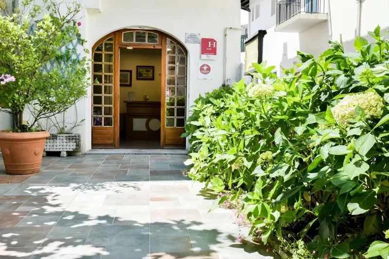 Entree d'un batiment blanc avec une arche en bois et des plantes vertes.