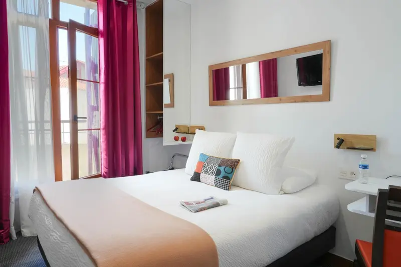 Une chambre lumineuse avec un lit double et un accès à un balcon.
