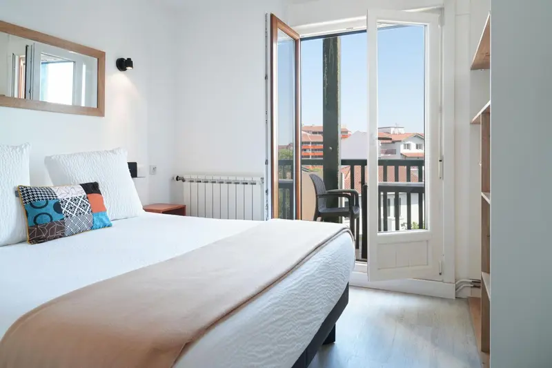 Une chambre lumineuse s'ouvre sur un balcon avec vue sur la ville.
