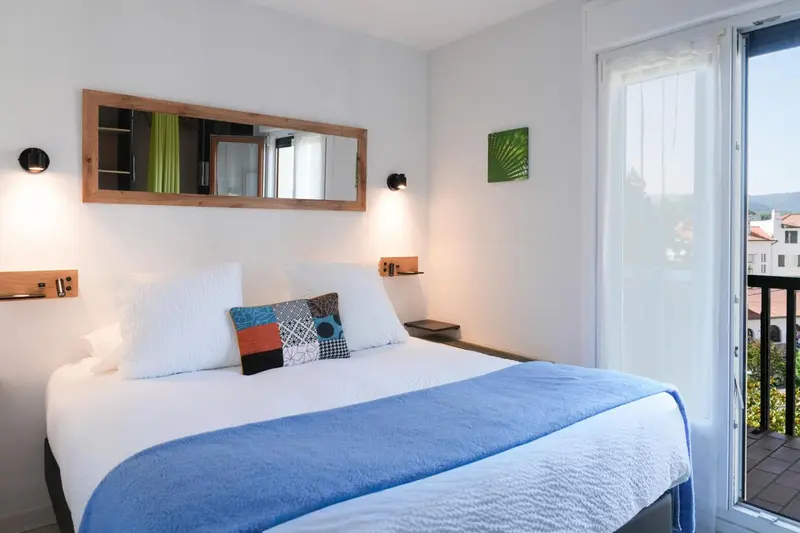 Une chambre lumineuse avec un lit fait et une vue sur l'extérieur.