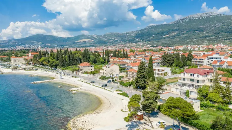 Vue aérienne d'une ville côtière avec une plage et des montagnes en arrière-plan.