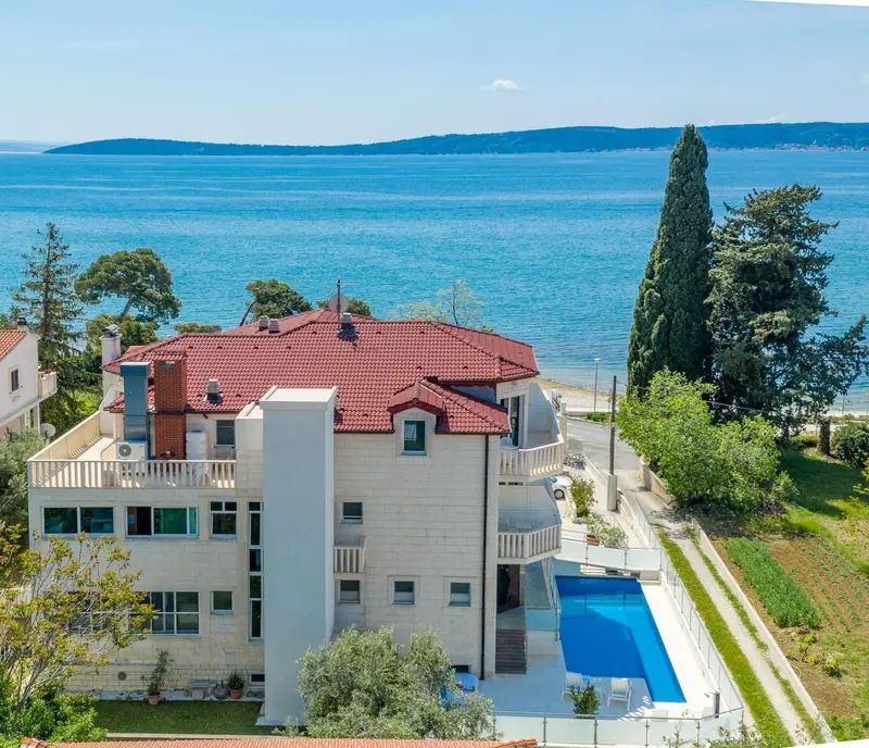 Vue aérienne d'une villa blanche avec piscine et végétation luxuriante face à la mer.