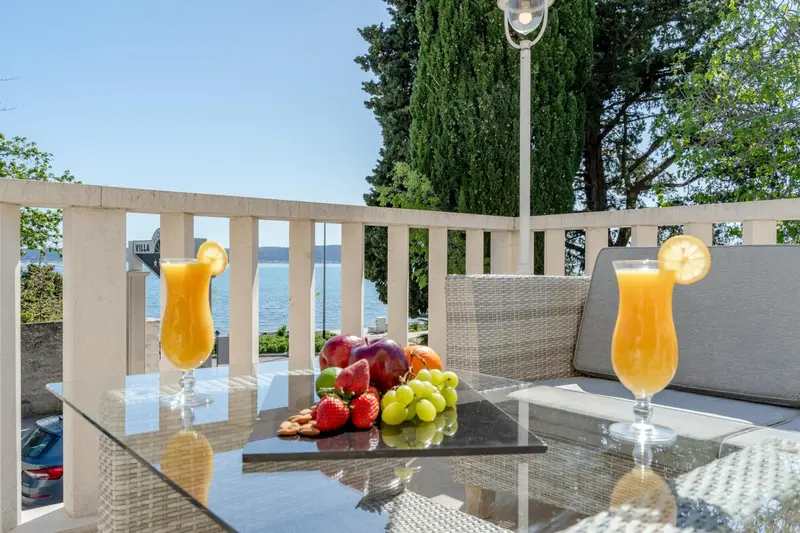 Une table basse avec des boissons et des fruits est mise en scène sur une terrasse ensoleillée.