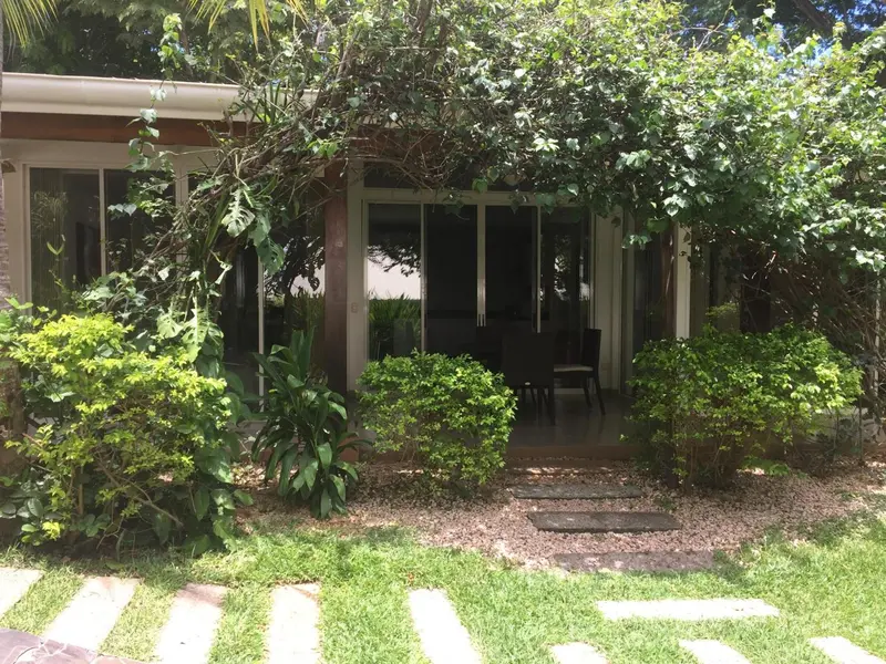 Façade d'un bâtiment entouré de végétation avec une terrasse ombragée.