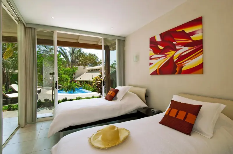 Chambre lumineuse avec deux lits simples et vue sur une piscine.