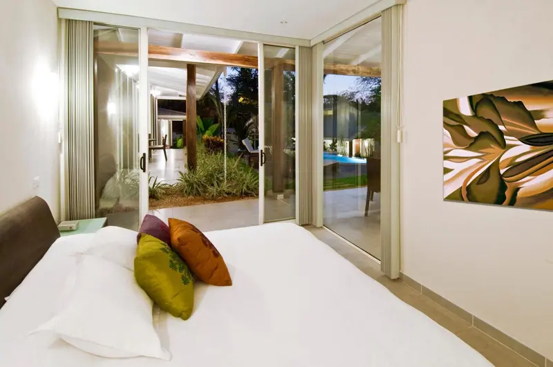 Une chambre lumineuse s'ouvre sur une terrasse donnant sur une piscine et un jardin.