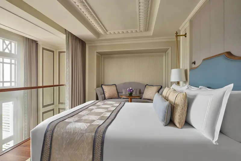 Chambre lumineuse avec un grand lit et un coin salon près d'une fenêtre.