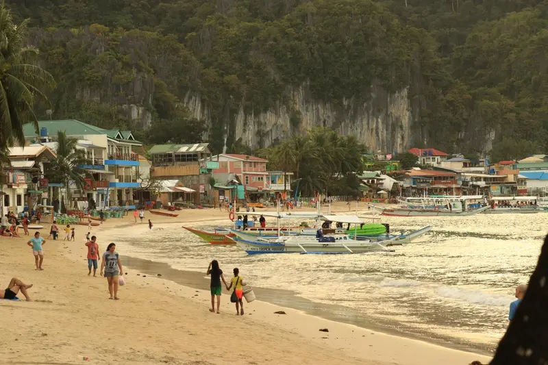 Une plage de sable clair bordée de bateaux colorés et de bâtiments.