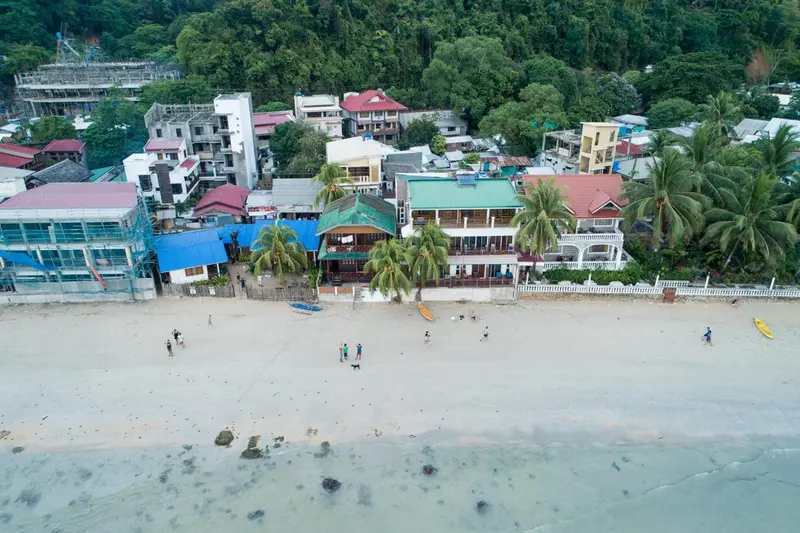 Vue aérienne d'une plage bordée de bâtiments et de palmiers.