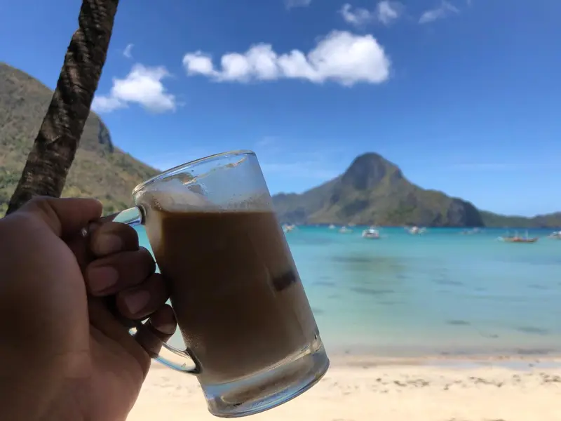 Une main tenant un verre de boisson sur une plage ensoleillée.