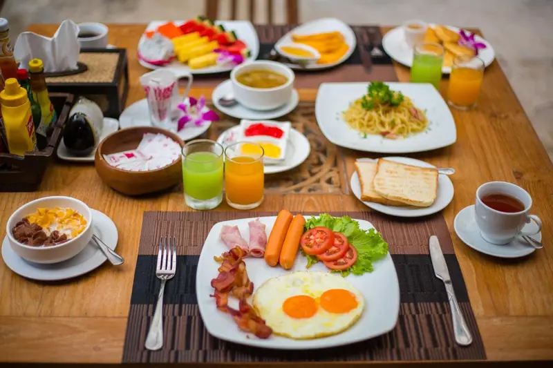 Table garnie d'un copieux petit-déjeuner avec fruits, œufs, viennoiseries et boissons.