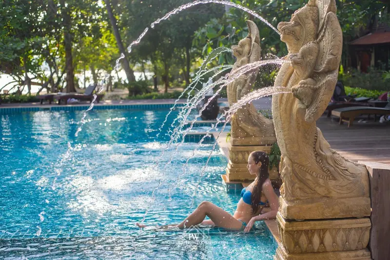 Une femme est assise au bord d'une piscine ornée de sculptures.