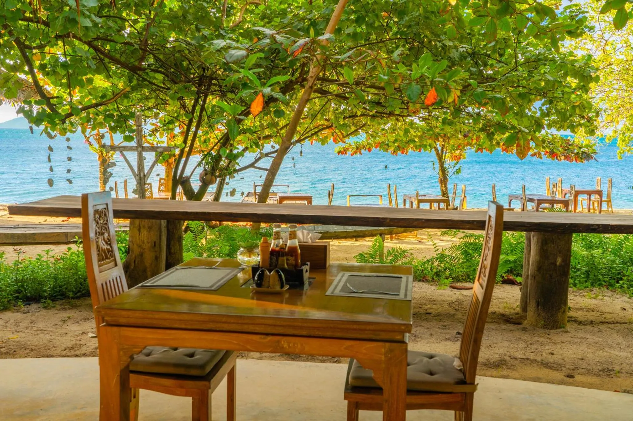 Une table est dressée à l'ombre d'arbres face à la mer.