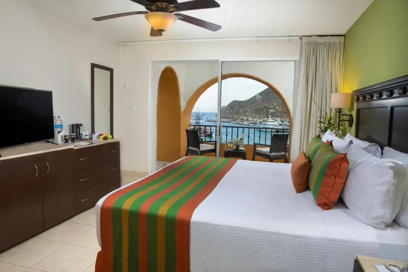 Chambre lumineuse avec un grand lit et un accès à un balcon offrant une vue sur la mer.
