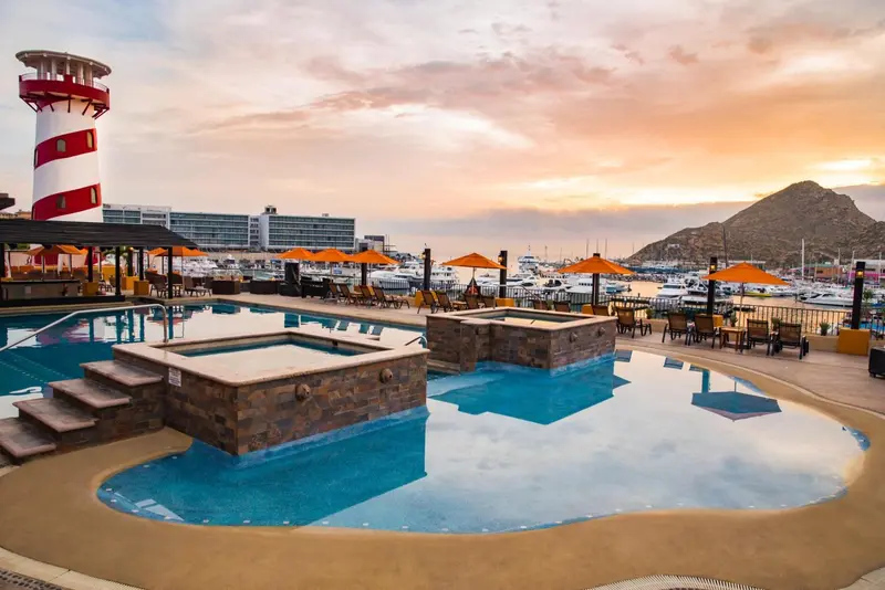 Piscine avec jacuzzi et transats au bord d'un port de plaisance au coucher du soleil.