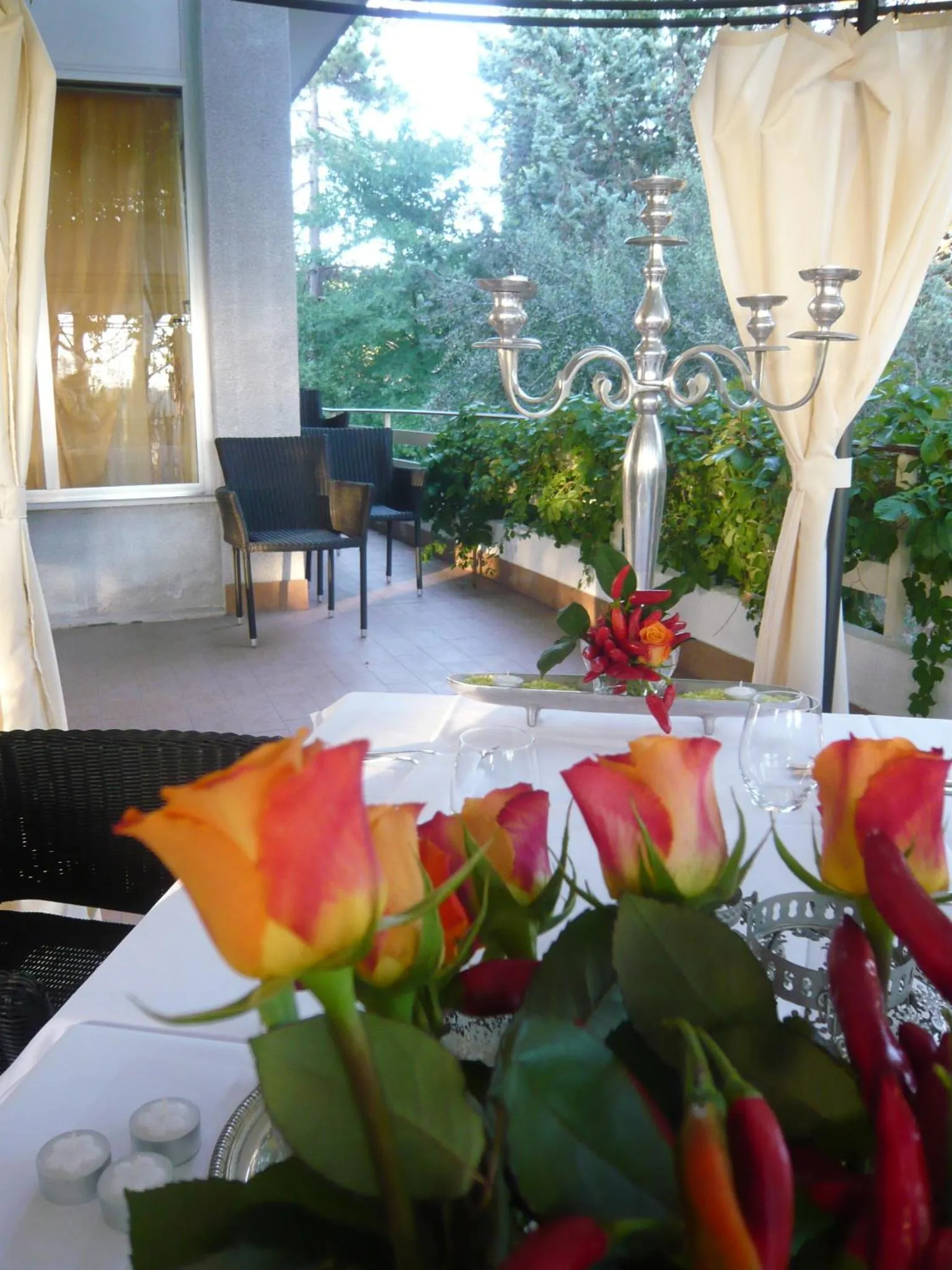 Table dressée avec des roses et des verres à vin sur une terrasse ombragée.