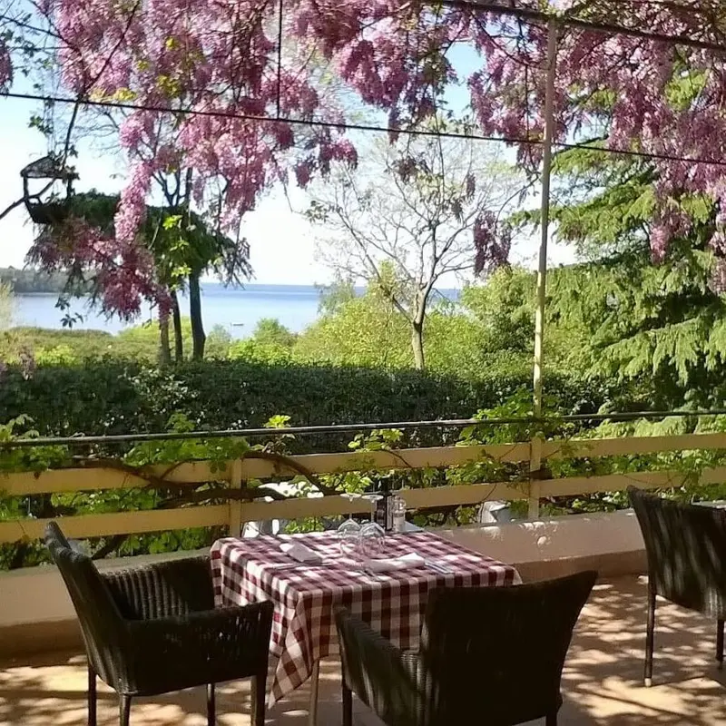 Une table est dressée sur une terrasse ombragée avec vue sur la mer.