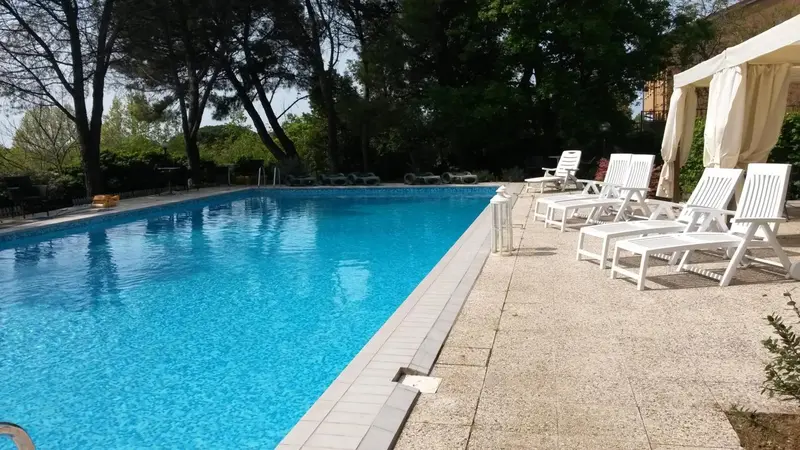 Une piscine rectangulaire bordée de transats blancs sous des parasols.