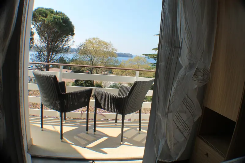 Deux fauteuils en osier sur une terrasse ensoleillée avec vue sur la mer et la végétation.
