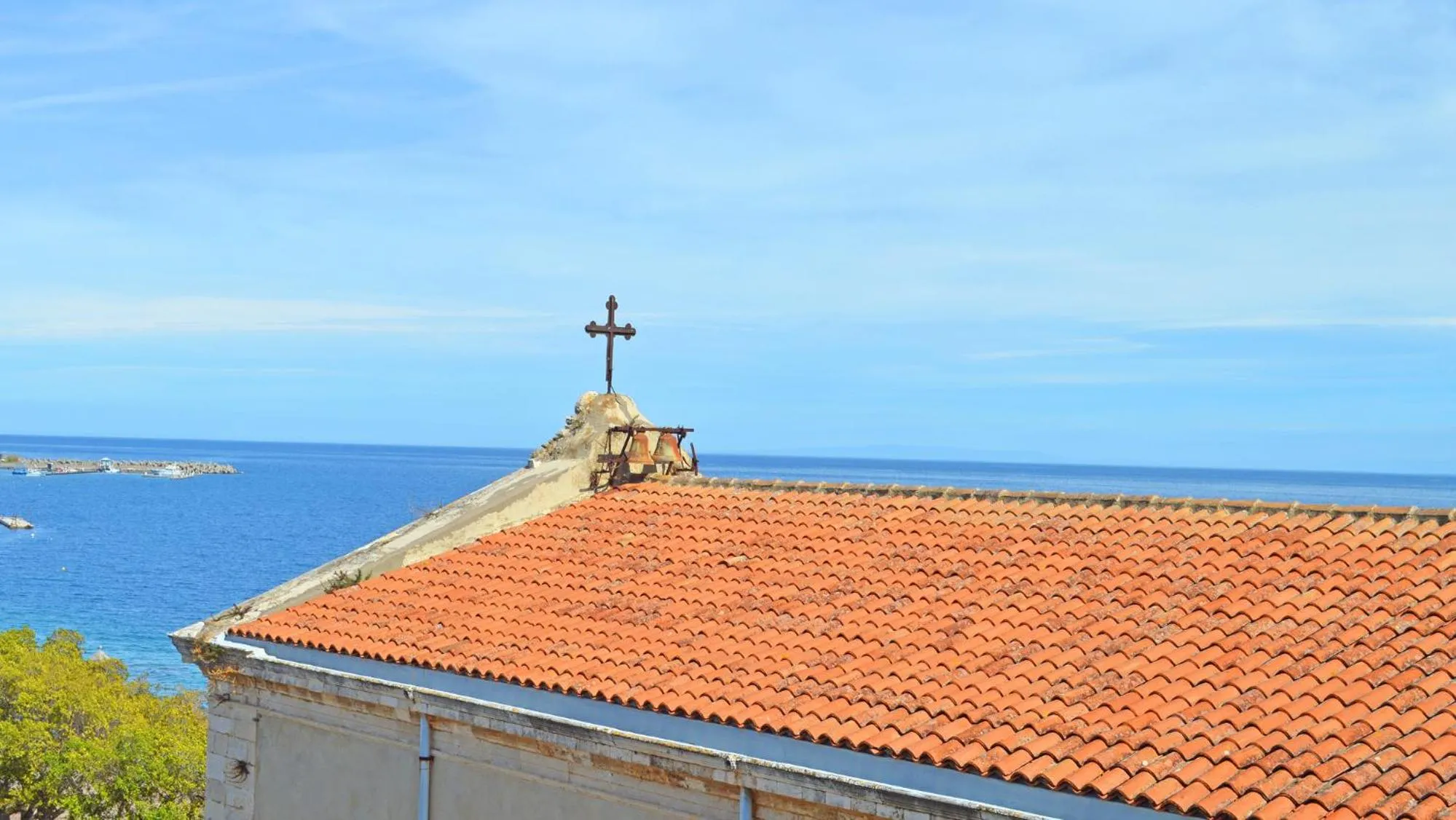 Toit en tuiles rouges avec une croix au sommet, vue sur la mer.