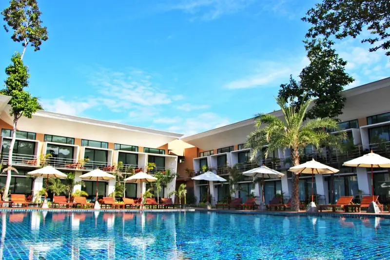 Bâtiment blanc et orange avec des parasols au bord d'une piscine turquoise.