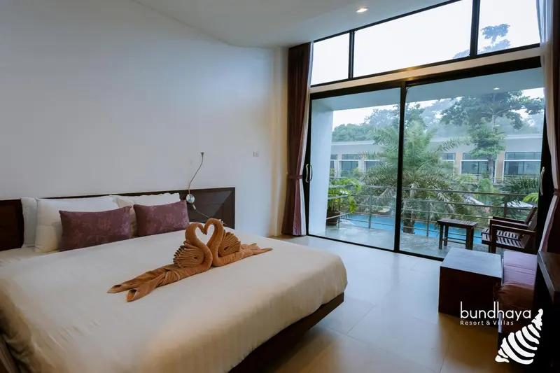 Une chambre lumineuse avec un grand lit et vue sur une végétation luxuriante.