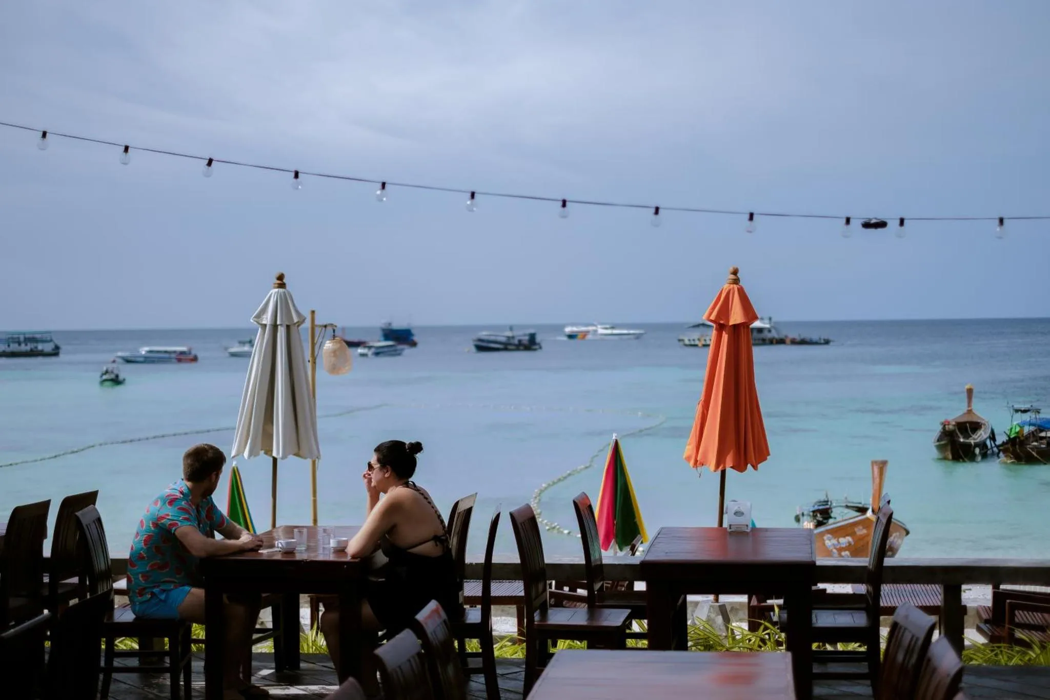 Deux personnes sont assises à une table sur une terrasse en bord de mer.