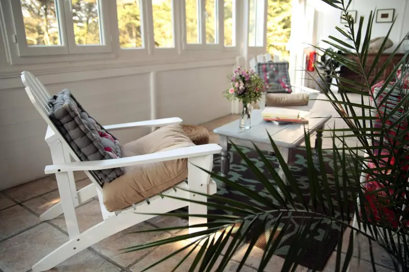 Un fauteuil en bois blanc avec coussins se trouve dans un espace lumineux et décoré de plantes.