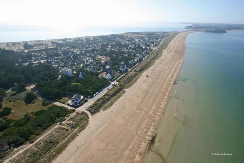Vue aérienne d'une plage de sable fin bordée de bâtiments et de végétation.