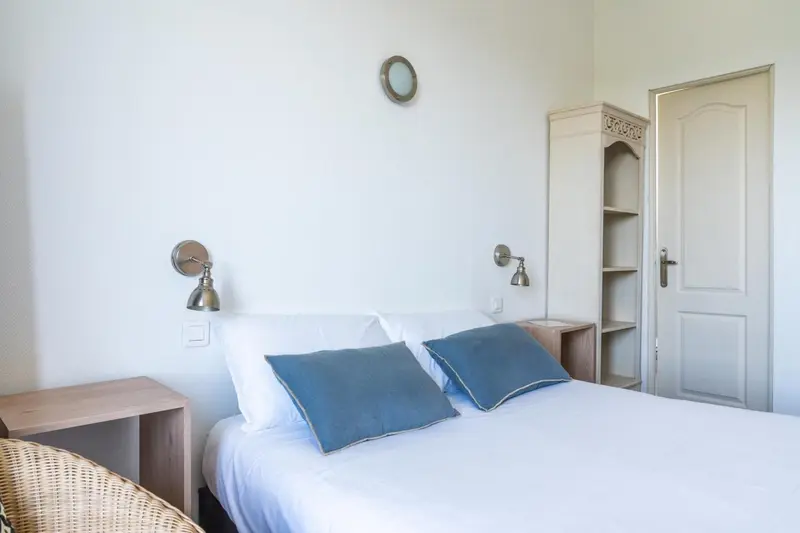 Une chambre lumineuse avec un lit recouvert d'une courtepointe bleue.