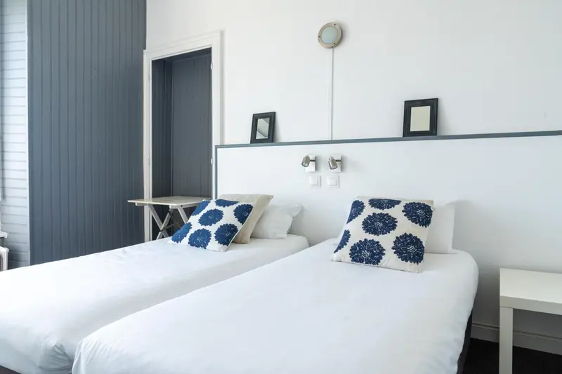 Deux lits simples avec oreillers bleus dans une chambre lumineuse.