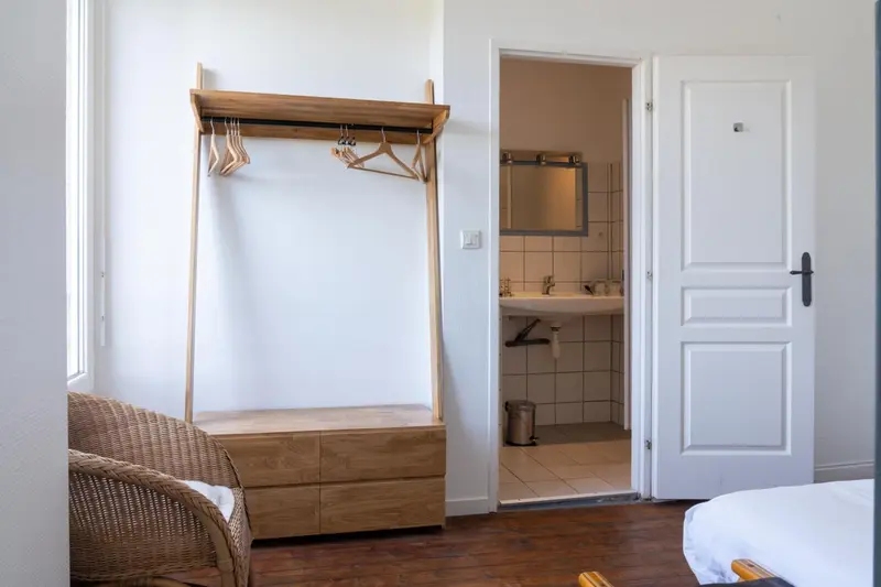 Une chambre lumineuse avec un porte-manteau en bois et l'ouverture vers une salle de bain.
