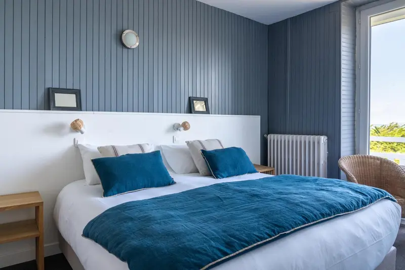 Une chambre lumineuse avec un grand lit recouvert d'une couverture bleue.