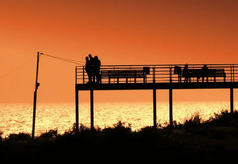 Une jetée sombre se prolonge sur une mer scintillante au coucher du soleil.