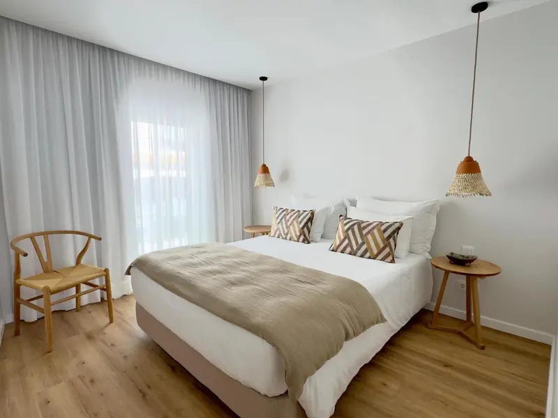 Une chambre lumineuse avec un grand lit et une chaise en bois.
