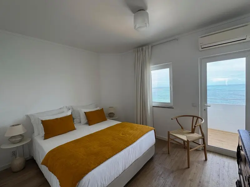 Une chambre lumineuse avec un lit recouvert d'une couverture jaune et une vue sur la mer.
