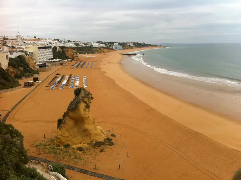Vue aérienne d'une plage de sable fin bordée de falaises et de vagues.