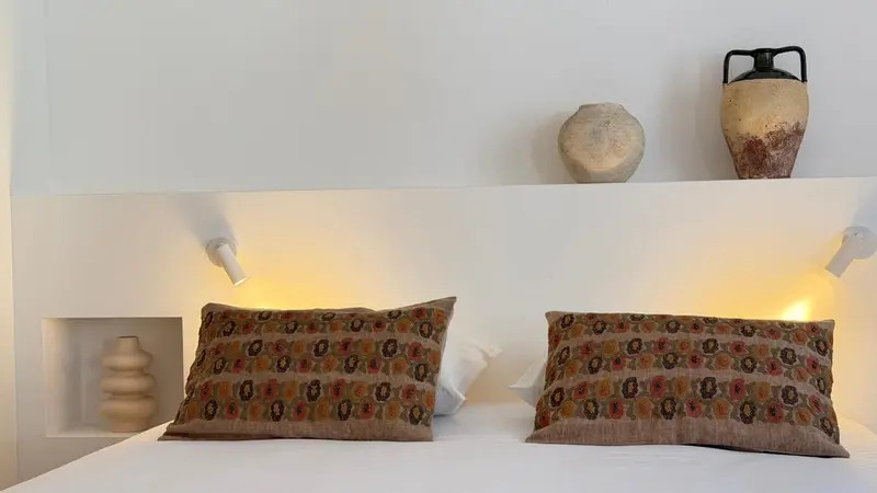 Un lit avec des coussins décoratifs et des luminaires muraux.