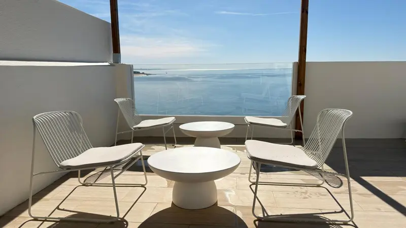 Mobilier d'extérieur blanc sur une terrasse ensoleillée avec vue sur la mer.