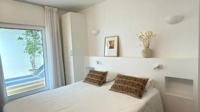 Une chambre lumineuse avec un lit double et une vue sur une terrasse.