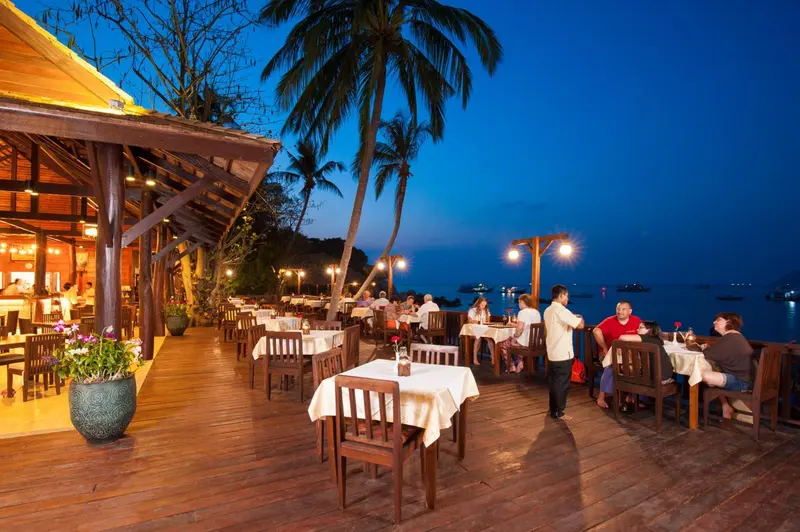 Terrasse de restaurant en bois avec tables nappées au bord de la mer.