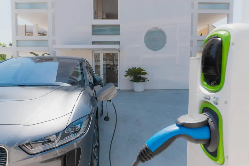 Une voiture électrique grise est en cours de recharge à une borne de couleur vive.