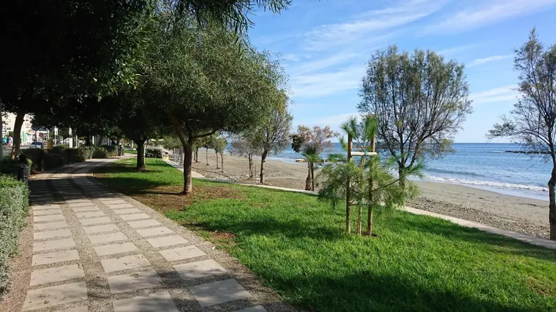 Allée piétonne bordée de verdure et longeant une plage de galets.