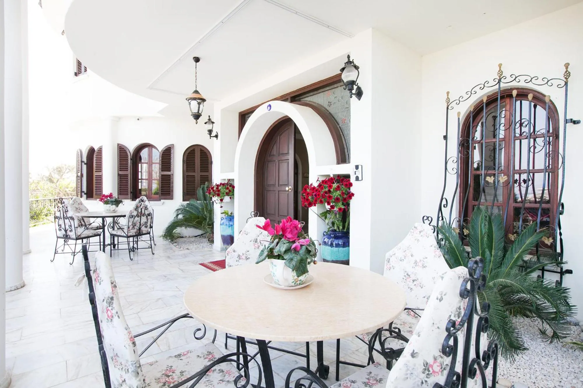 Terrasse ombragée avec tables et chaises fleuries devant une entrée ornée.