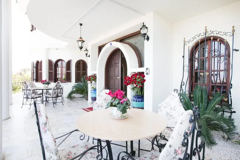 Terrasse ombragée avec tables et chaises fleuries devant une entrée ornée.