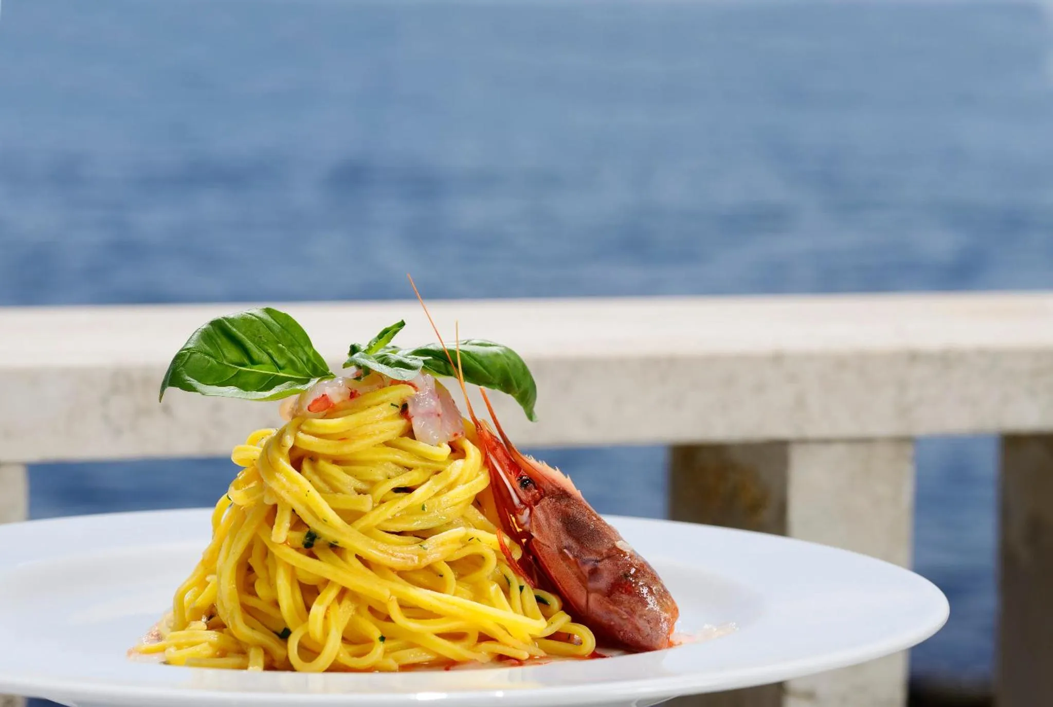 Assiette de pâtes aux fruits de mer sur une table en extérieur avec vue sur la mer.