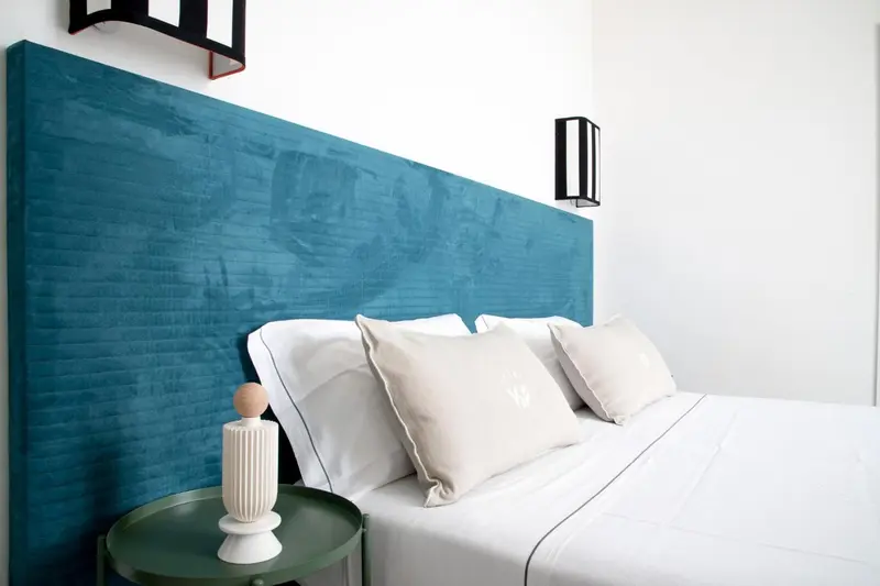 Une chambre lumineuse avec un grand lit recouvert de linge blanc et une tête de lit turquoise.