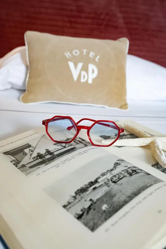 Un livre ouvert et des lunettes de soleil reposent sur un lit blanc avec un oreiller décoratif.