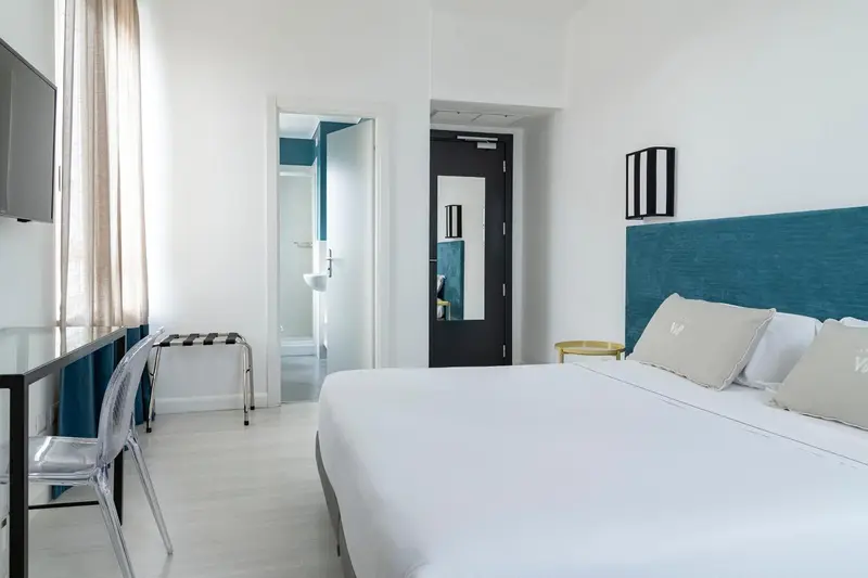 Une chambre lumineuse avec un lit blanc et un bureau.