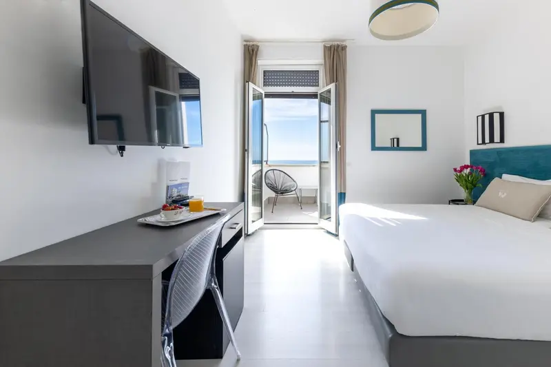 Une chambre lumineuse avec un lit blanc et un balcon ouvert sur la mer.